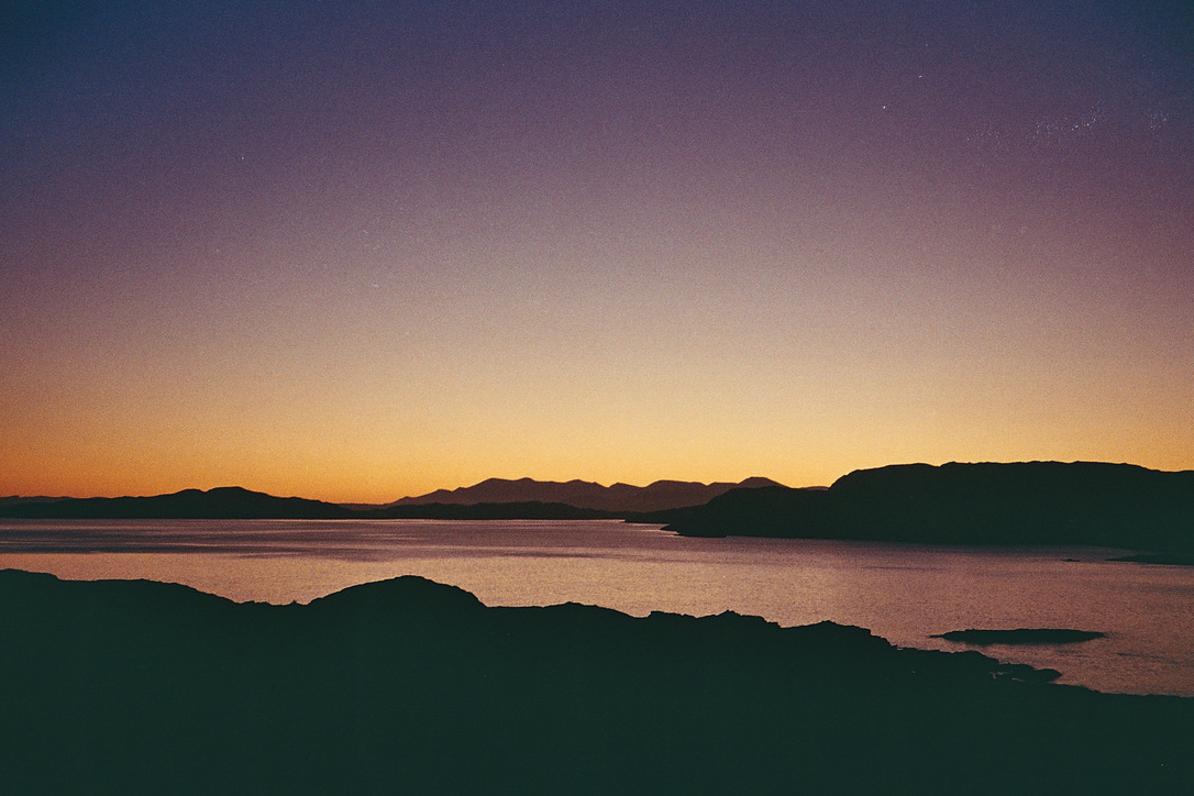 An orange and violet evening sky over water and dark headlands